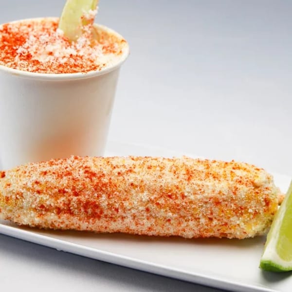 Elote, Mexican street corn, on a white plate with a side of esquites in a cup.
