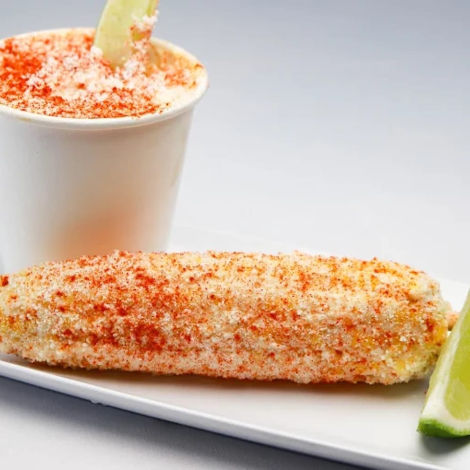 Elote, Mexican street corn, on a white plate with a side of esquites in a cup.