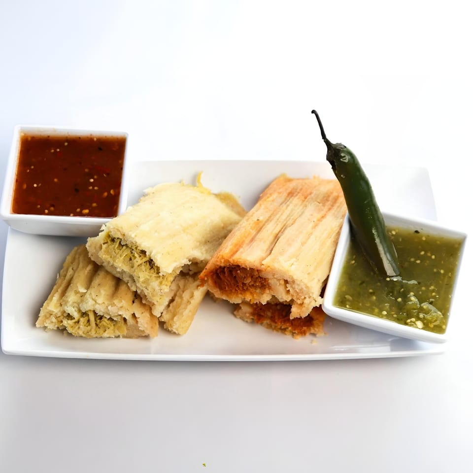 Two Mexican tamales, one chicken and one pork, with red and green salsa on a white plate.