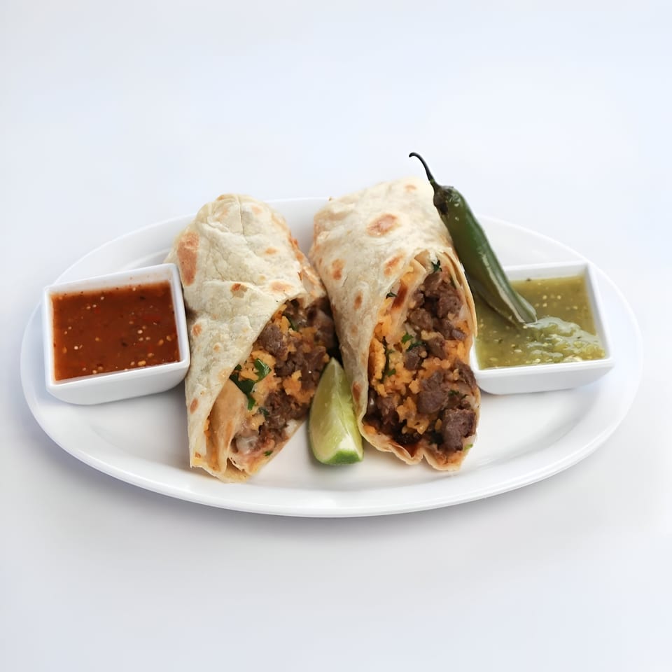 Two Mexican burritos, a lime wedge, a jalapeño, and two salsa bowls on a white plate.